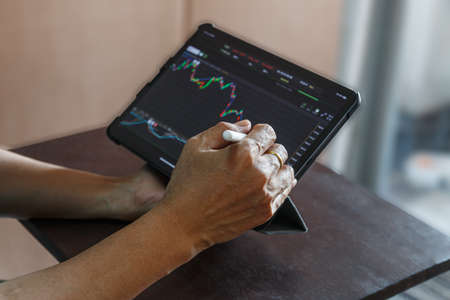 Businessman checking stock market data candlestick chart on application in tablet.With homeの写真素材