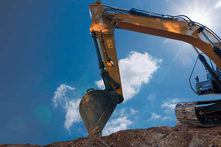Excavator digging the soil In the construction site area  on blue sky and sun backgroundの写真素材