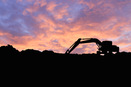 Excavators silhouette are digging soil with bucket lift up in the construction site on sky ...