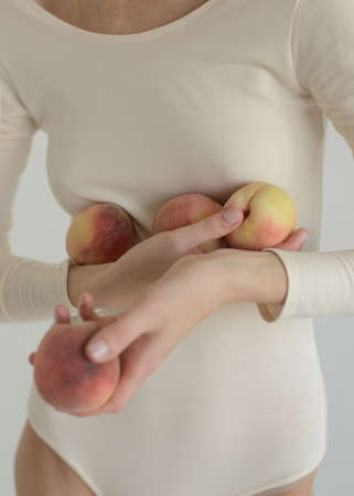 Girl in white body on white neutral background. Redhead girl with curly hair, blue eyes and big lips. natural. Soft and harmonic portrait. Pomegranate and peaches in hands. Skin problems, cosmetologyの写真素材