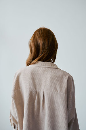 Portrait of young amazing redhead girl in beige shirt on neutral background. Long wavy healthy hair....