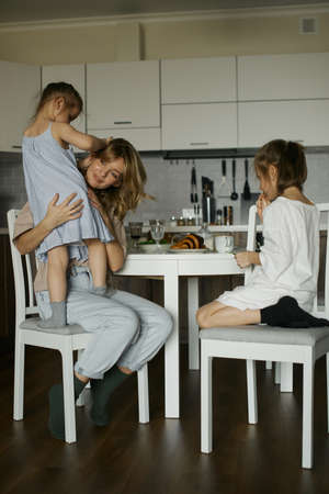 Young beautiful mother with two pretty daughters in the kitchen. Happy family breakfast. Stylish interior. good relationships. Funny kids. love and care. Europeans. Live and natural pictureの写真素材