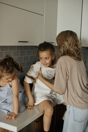 Young beautiful mother with two pretty daughters in the kitchen. Happy family breakfast. Stylish...