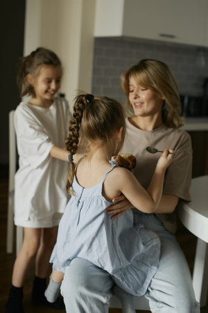 Young beautiful mother with two pretty daughters in the kitchen. Happy family breakfast. Stylish...
