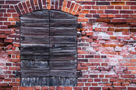 Fragment of a warehouse with crumbling brick wall and old wooden shutters closedの写真素材