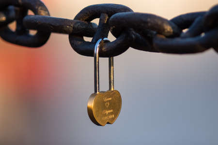 A heart shaped love lock hanging on a chain in a colourful backgroundの写真素材