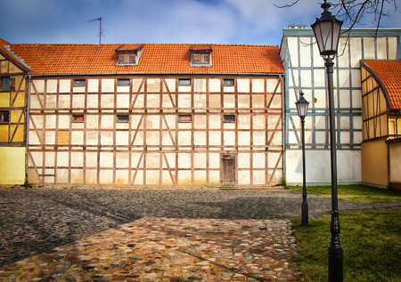 Half-timbered buildings with small windows surrounding a little stone paved square in the old town of the cityの写真素材