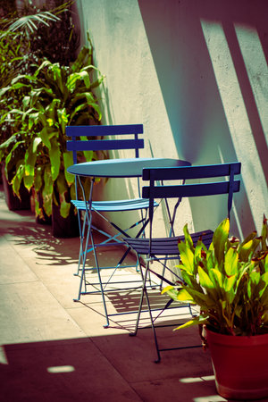 Outdoor blue bistro furniture set on a sunny patio with lush green plants and modern architectureの写真素材