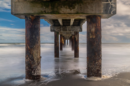 Captured along Floridaâs east coast, this long-exposure seascape reveals the motion of waves rolling beneath a pier at the edge of autumn. The interplay of light, shadow, and structure speaks to the ongoing rhythm between nature and manmade form.の写真素材
