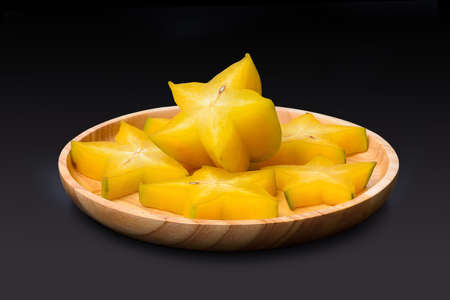 Slice of yellow star fruit on the wooden round tray isolate on black backgroundの写真素材