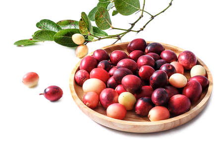 Karonda or carunda fruit in the round wooden tray with green leaves and berries, isolated on white backgroundの写真素材