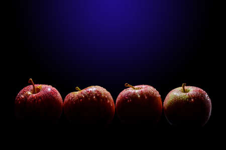 Four red apples in row with light and shadows on black and blue backgroundの写真素材
