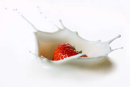 Red strawberry fruits falling into the milky splash