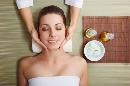 Beautiful young woman lying relaxed in a spa salon and receiving facial massage. Beauty treatment.の写真素材