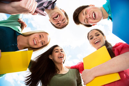 Group of smiling students staying together and looking at camera on sky backgroundの写真素材