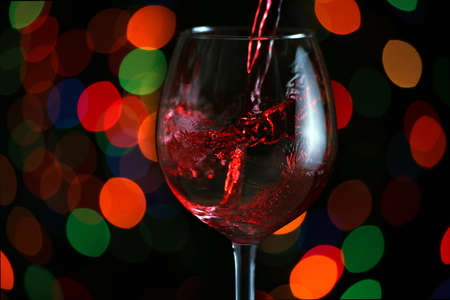 Beautiful splash of red wine in a glass against the festive lightsの写真素材
