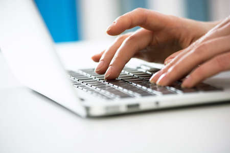 Close-up of hands of businesswoman typing on a laptop. View through blindsの写真素材