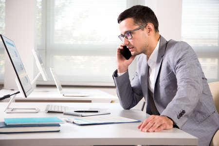Young handsome businessmantalking on the phone in an officeの写真素材