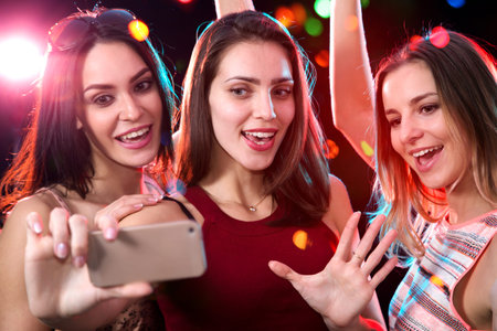 Smiling girls with smartphone taking selfie in a night club
