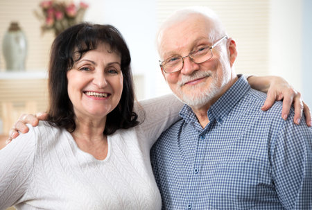 Portrait of a happy cute elderly couple cuddling and looking at camera