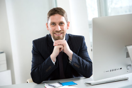 Young handsome businessman working with computer at office smiling at camera