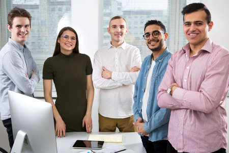 Multy-ethnic group of young business people working while standing at the office desk and smiling at cameraの写真素材