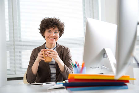 Portrait of a pretty business woman with tea mug at workplace in officeの写真素材