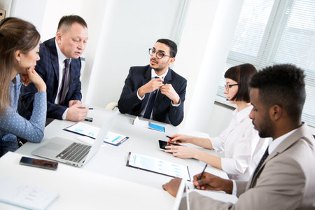 International group of business people working and communicating sitting near office desk together.