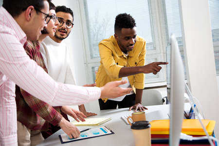 Multy-ethnic group of creative business people standing at the office desk and working with computerの写真素材