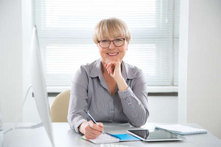 Portrait of mature business woman looking at camera at workplace in an officeの写真素材