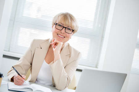 Portrait of mature business woman looking at camera at workplace in an officeの写真素材