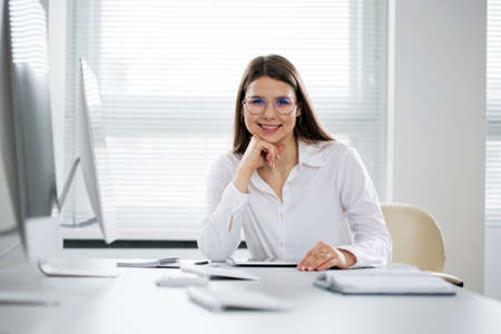 Portrait of pretty business woman looking at camera at workplace in an officeの写真素材
