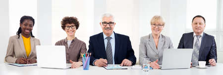 Multy-ethnic group of young business people working while sitting at the office desk and smiling at cameraの写真素材