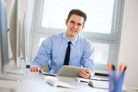 Portrait of happy young businessman working with tablet computer at officeの写真素材