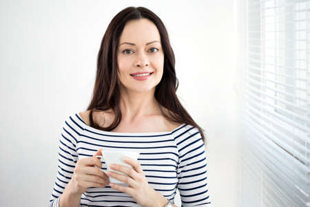 Portrait of a beautiful business woman with a cup of tea by the windowの写真素材