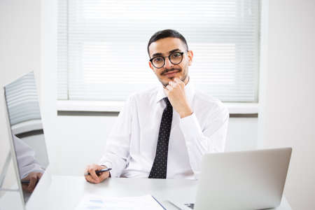 Happy handsome arab businessman smiling while looking at camera in officeの写真素材