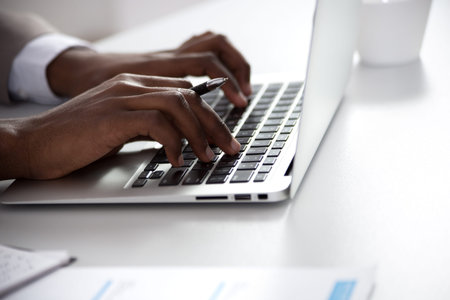 Close-up of hands of african-american businessman typing on a laptop. View through blindsの写真素材