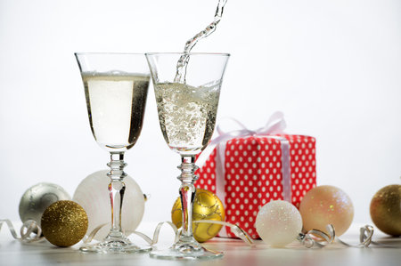 Beautiful splash of champagne glasses and Christmas gifts and balls on a white backgroundの写真素材
