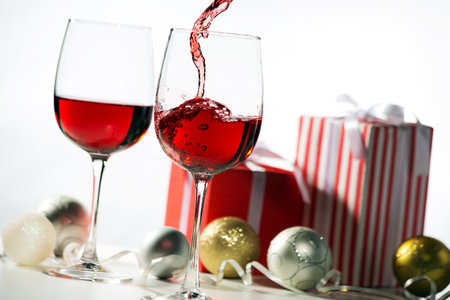 Beautiful splash of red wine in crystal glasses on the background of Christmas gifts and Christmas ballsの写真素材