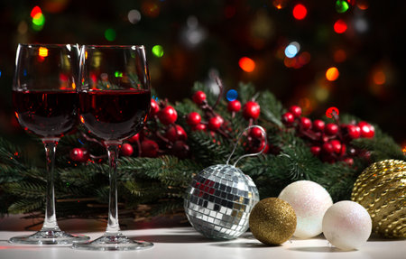 Crystal glasses of wine and Christmas balls on the background of Christmas lights and Holly red berriesの写真素材