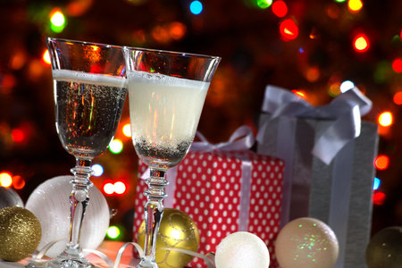 Beautiful splash of champagne glasses and Christmas gifts on the background of Christmas lightsの写真素材
