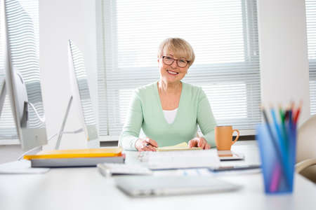 Portrait of mature business woman looking at camera at workplace in an officeの写真素材