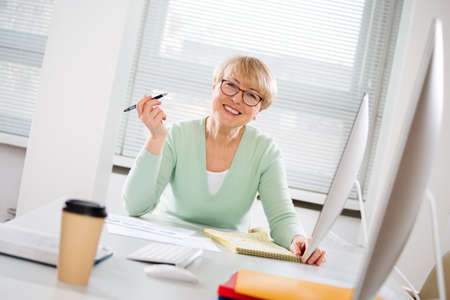 Portrait of mature business woman looking at camera at workplace in an officeの写真素材