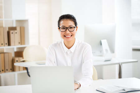 Asian business woman smiling at camera at workplace in an officeの写真素材