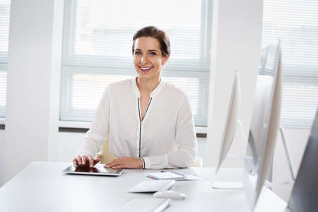 Portrait of pretty business woman looking at camera at workplace in an officeの写真素材