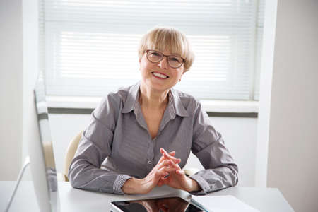 Portrait of mature business woman looking at camera at workplace in an officeの写真素材