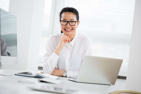 Asian business woman smiling at camera at workplace in an officeの写真素材