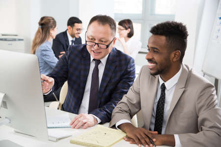 African american and Asian businessmen discussing new project in office using computerの写真素材