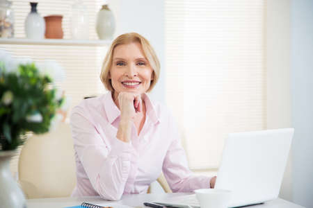 Portrait of mature business woman looking at camera at workplace in an home officeの写真素材