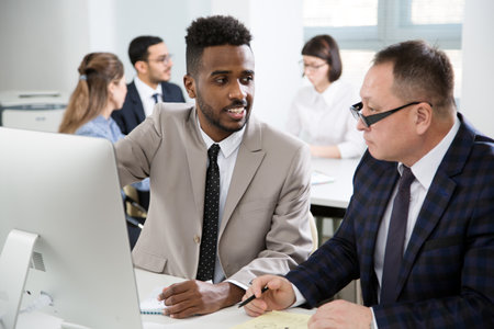 African american and Asian businessmen discussing new project in office using computerの写真素材